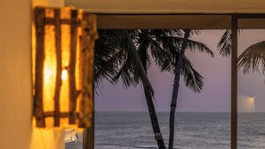 Un balcón con plantas en macetas, con vista a una playa con palmeras y al océano.
