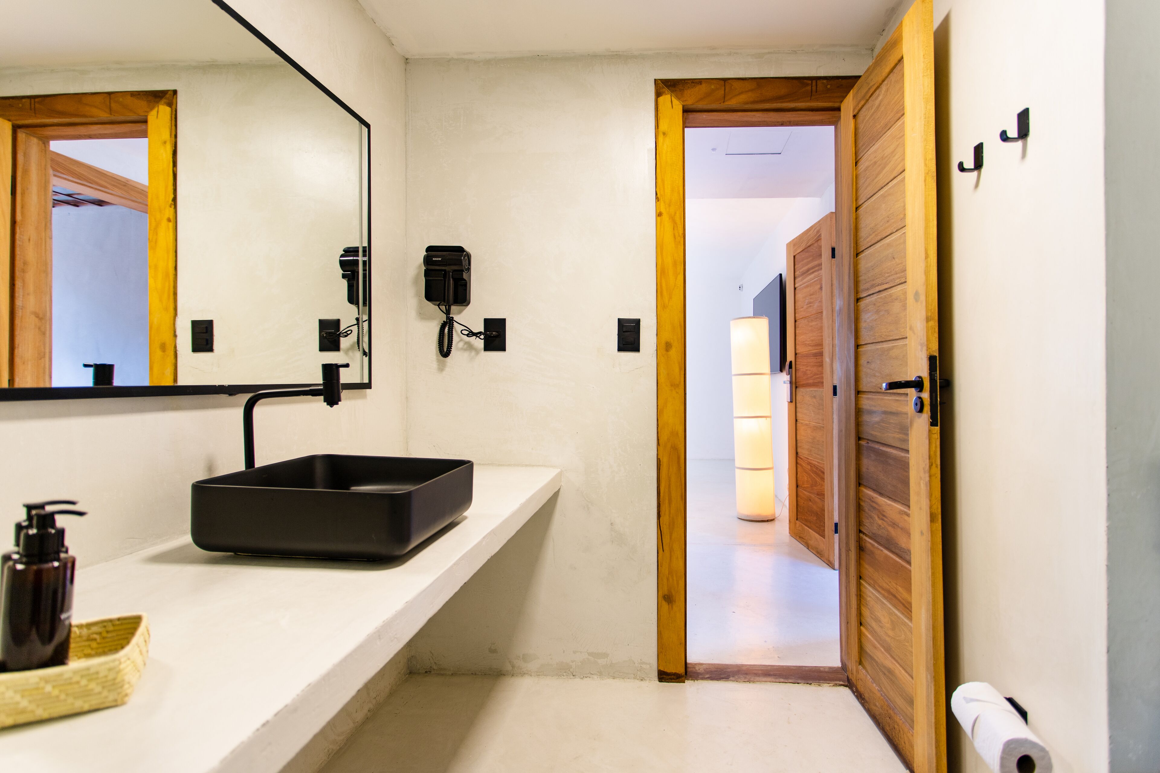 Un baño moderno con un lavamanos blanco, un espejo, un teléfono negro y una puerta de madera.