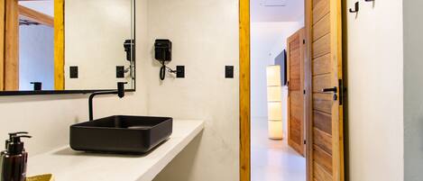 A modern bathroom with a white sink, a mirror, a black telephone, and a wooden door.