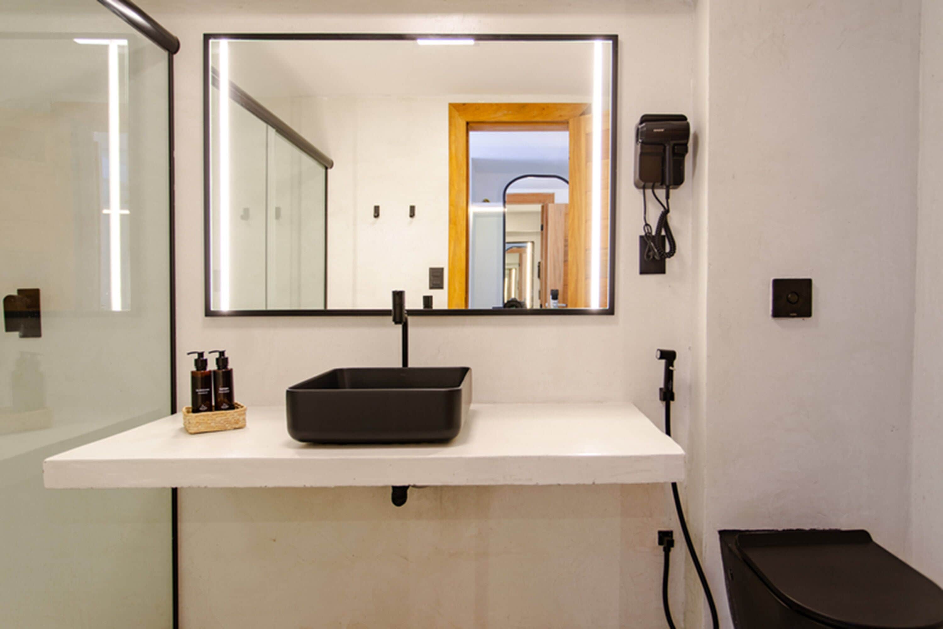 Un bagno con uno specchio grande, un lavandino nero e un piccolo cesto con articoli da toilette.