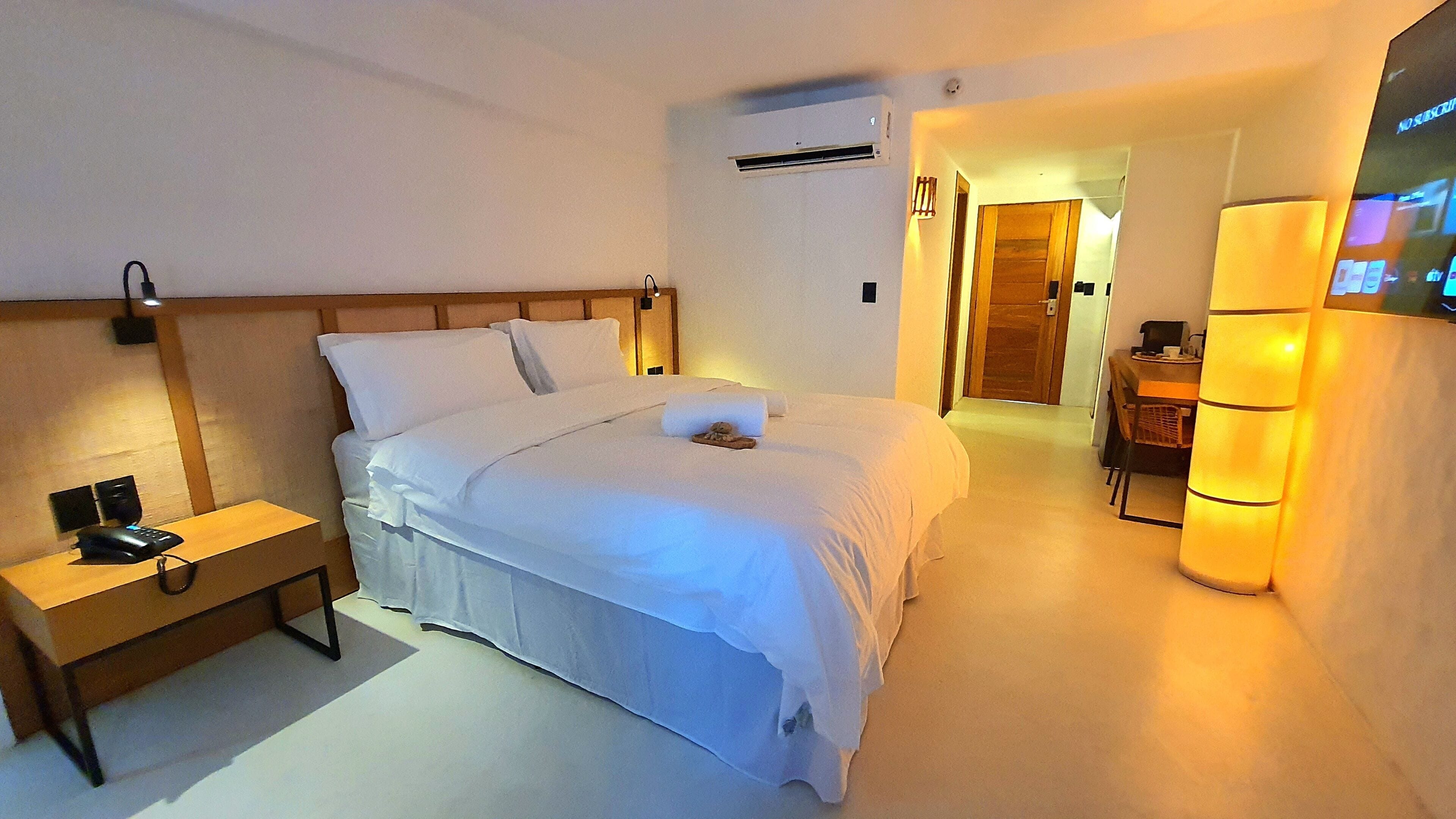 A hotel room with a bed, bedside table, lamp, and a TV on a stand.