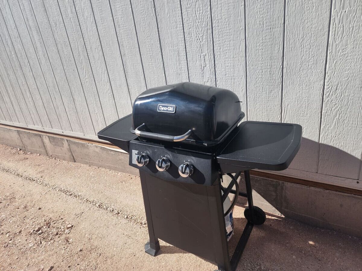 A portable grill with a control panel and a built-in smoker, placed outdoors against a wooden fence.