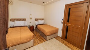 A bedroom with two beds, a wooden wardrobe, a bedside table, and a hanging light fixture.