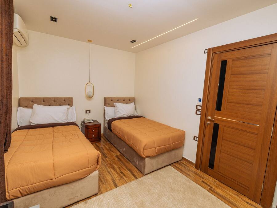 A bedroom with two beds, a wooden wardrobe, a bedside table, and a hanging light fixture.
