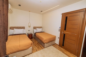 A bedroom with two beds, a wooden wardrobe, a bedside table, and a hanging light fixture. - White Pyramids inn  (Giza)