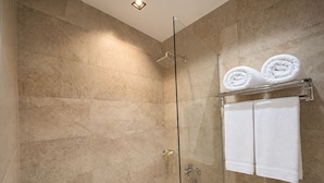 Douche met glazen wand, beige tegels en twee witte handdoeken op een metalen rek.