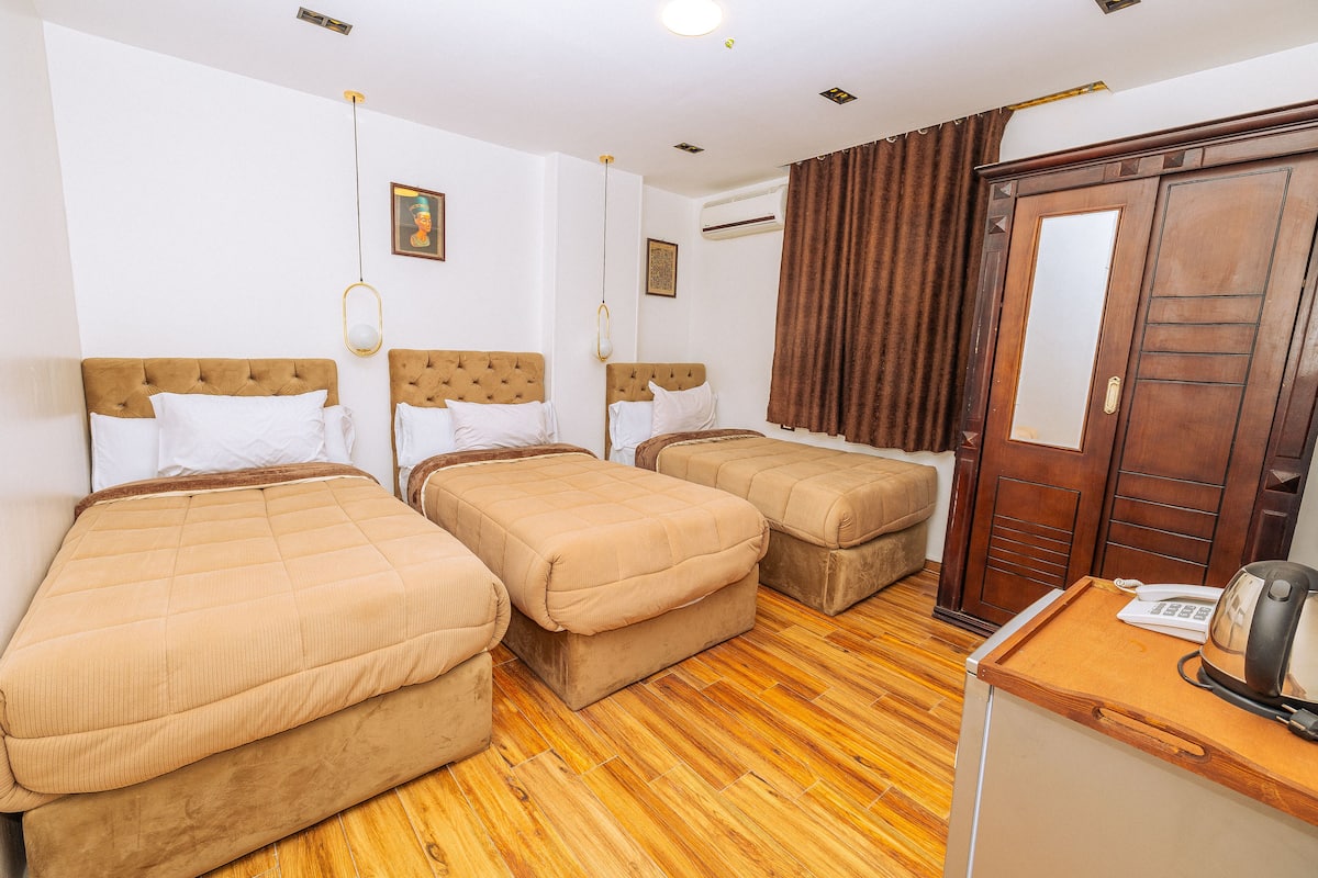 A hotel room with two single beds, a wooden wardrobe, a small desk with a telephone, and a mirror.