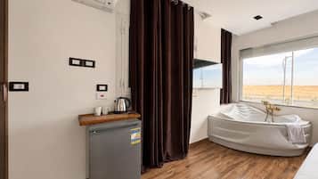 A hotel room with a bed, a small kitchenette, a window with a view of the desert, and a shower area.