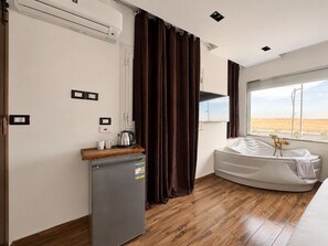 Habitación de hotel con cama, un pequeño rincón de cocina, ventana con vista al desierto y zona de ducha.