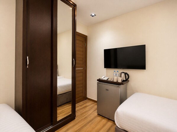 A hotel room with a wardrobe, a bed, a desk with a coffee maker, a kettle, and a flat-screen TV.