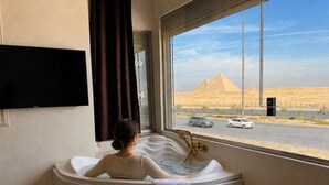 A person relaxing in a bathtub with a view of the pyramids through a large window. - White Pyramids inn  (Giza)