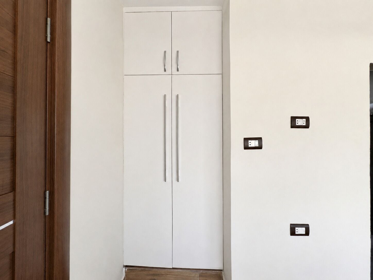 Une armoire blanche à deux portes et un plancher en bois.