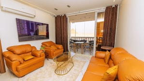 A living room with orange sofas, a glass coffee table, and a flat-screen TV mounted on the wall.