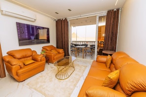 A living room with orange sofas, a glass coffee table, and a flat-screen TV mounted on the wall. - White Pyramids inn  (Giza)