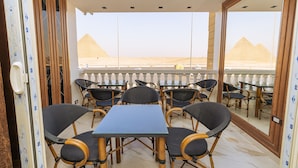 A balcony with a table and chairs, a view of the pyramids, and a patterned wall.