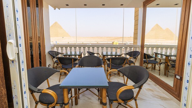 A balcony with a table and chairs, a view of the pyramids, and a patterned wall. - White Pyramids inn  (Giza)