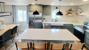 A modern kitchen with a central island, pendant lighting, and a view of the outdoors. - Our new lovely home ready for you (Garden City)