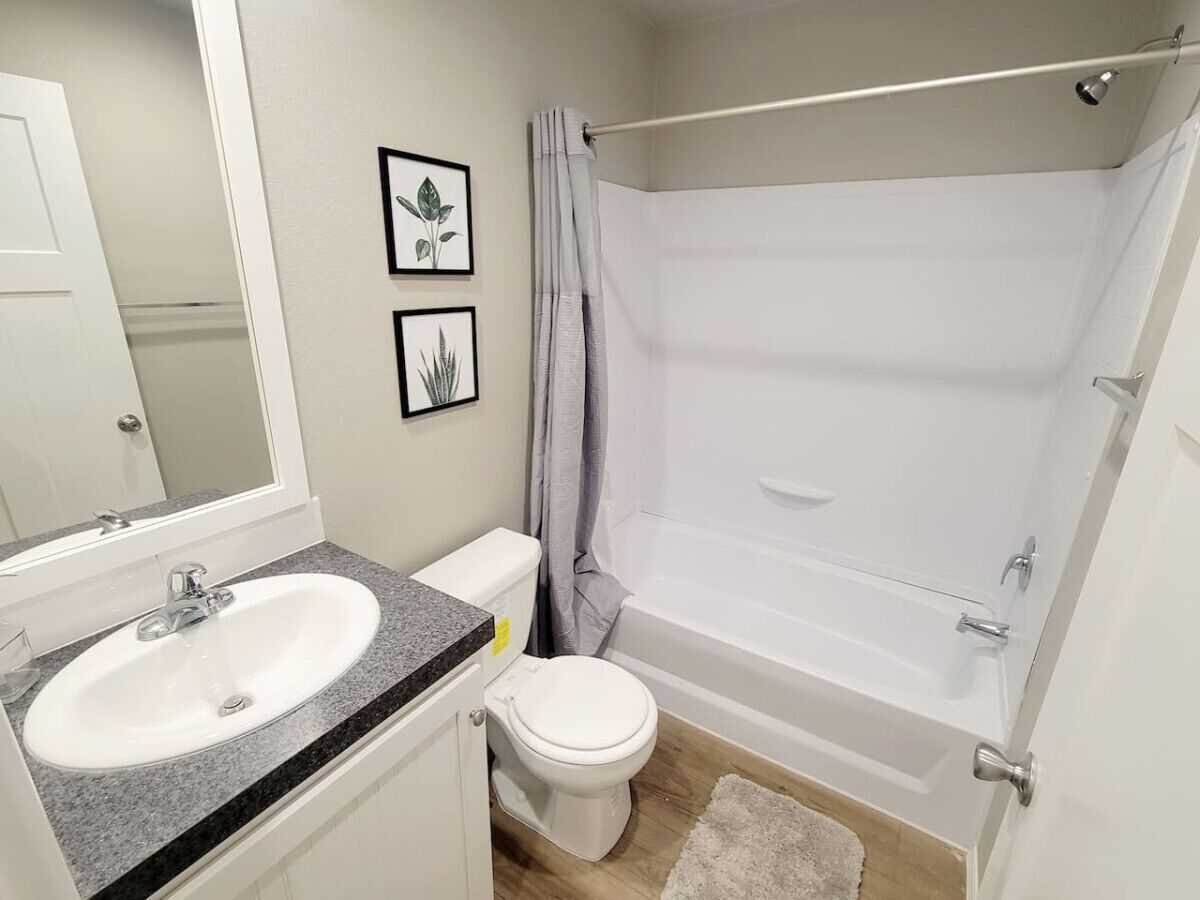 A bathroom with a white sink, toilet, and bathtub. There are framed botanical prints on the wall.