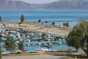 Uma marina com vários barcos atracados, uma estrada com veículos e montanhas ao fundo.