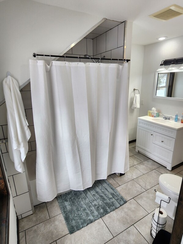 Une salle de bain avec un rideau de douche, un lavabo, un miroir et des toilettes.