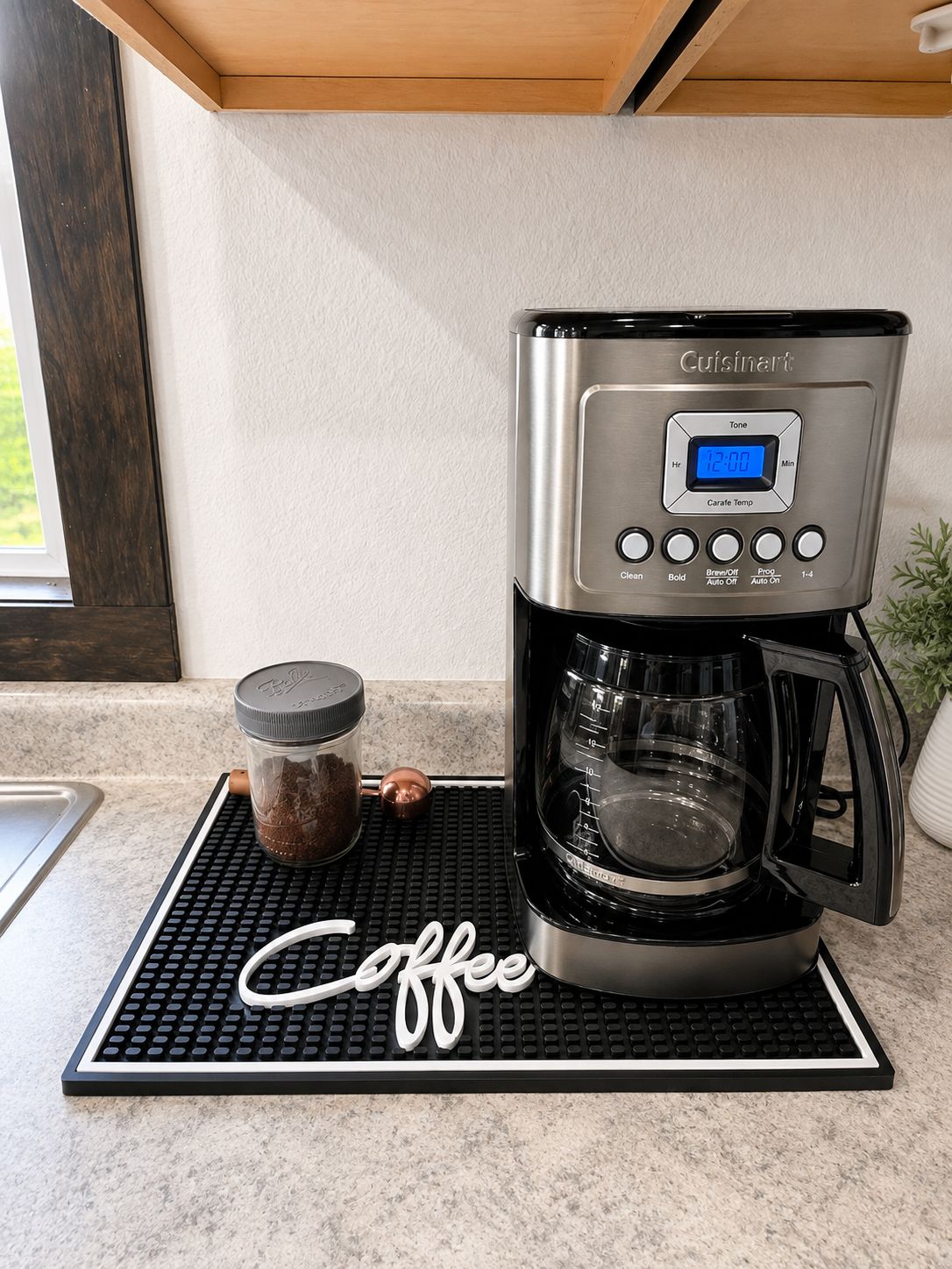 Une machine à café Cuisinart posée sur un plan de travail de cuisine, avec un support pour les capsules de café et un bocal de café moulu.