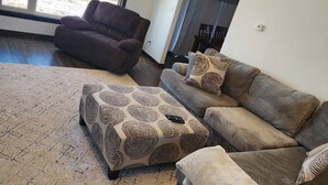Ein modernes Wohnzimmer mit einem braunen Ledersofa, einem gemusterten Hocker und einem großen Teppich.