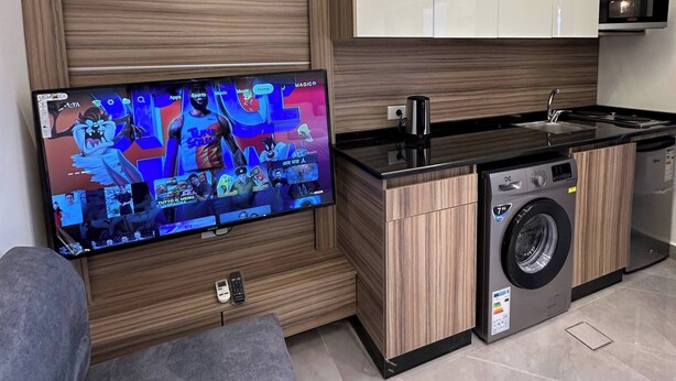 A modern kitchen with a built-in washing machine, a flat-screen TV mounted on the wall, and wooden cabinetry. - X Antica Jabalal-lwebdeh (Amman)