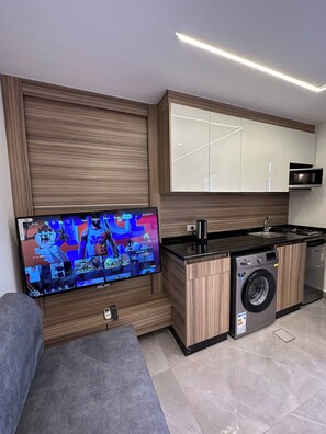Une cuisine moderne équipée d’un lave-linge encastré, d’un téléviseur à écran plat fixé au mur et de meubles de rangement en bois.