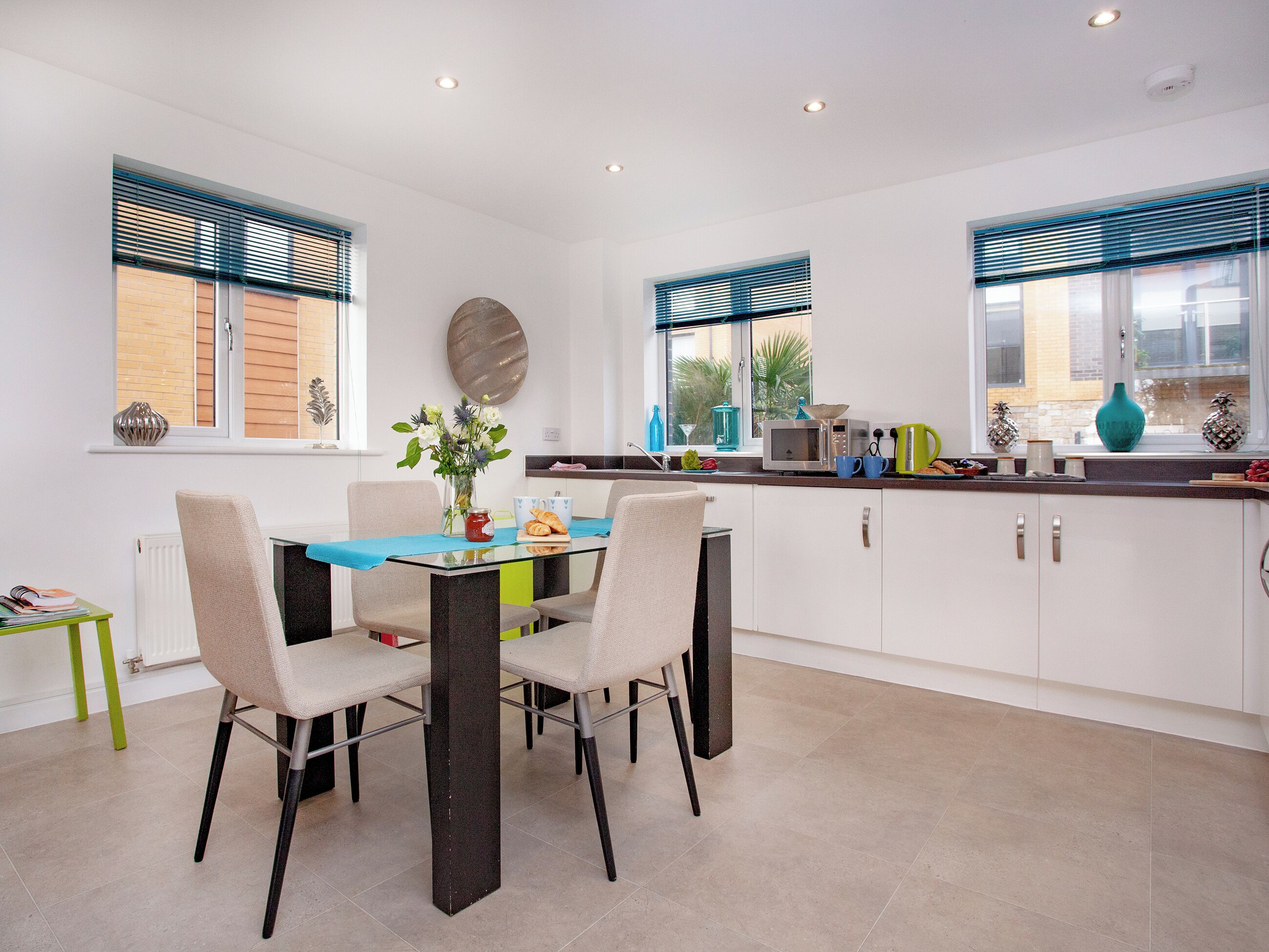 A modern kitchen with white cabinets, a dining table with chairs, and a window with blinds.