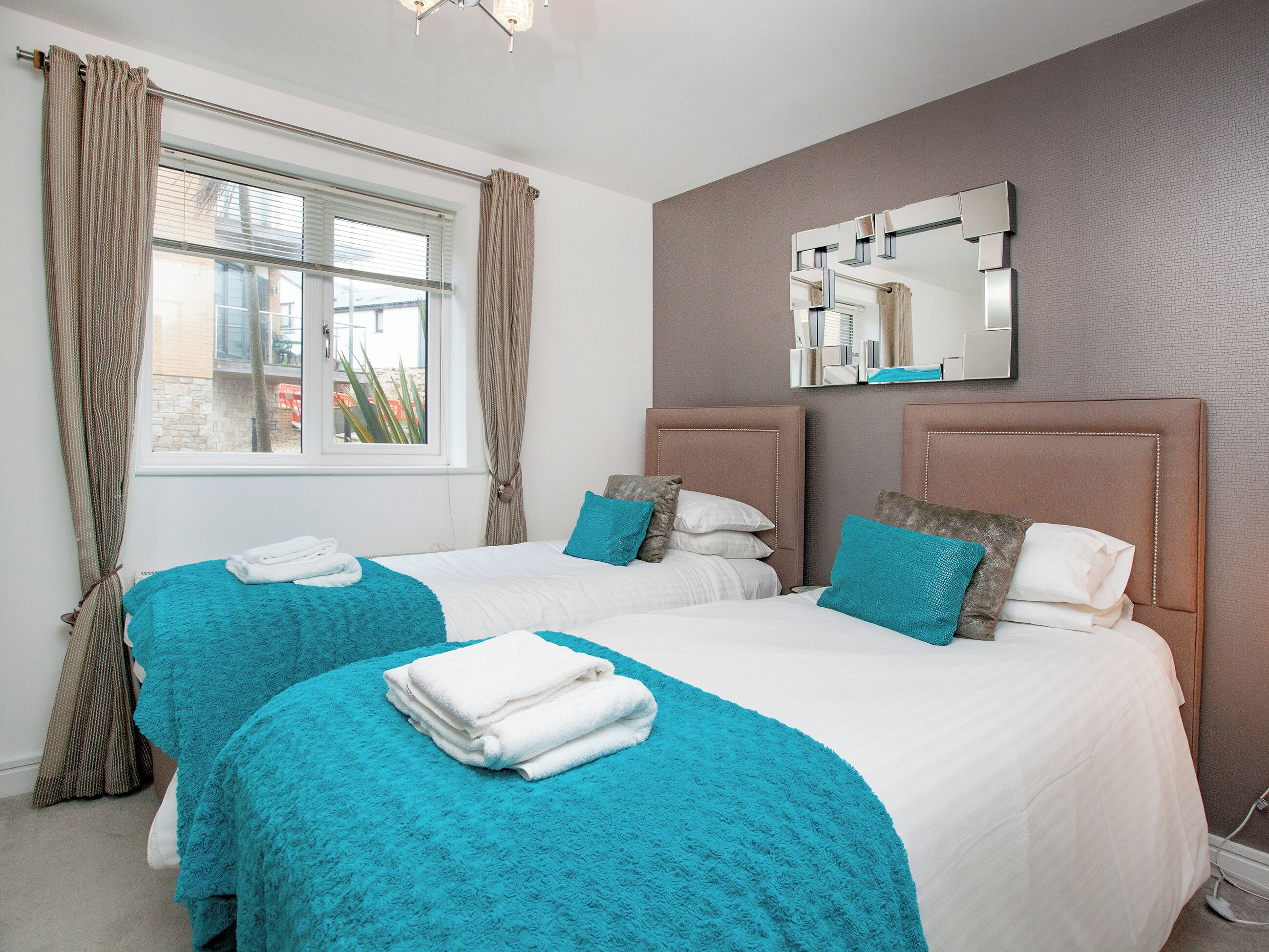 Habitación de hotel con dos camas, una ventana con cortinas, un espejo y un estante en la pared.