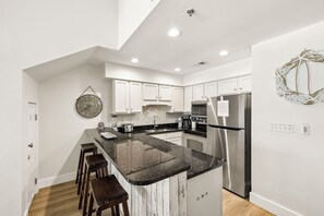 Une cuisine moderne avec des meubles blancs, un plan de travail en granit, des appareils électroménagers en acier inoxydable et un élément décoratif mural.