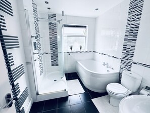Un baño moderno con ducha de vidrio, bañera independiente y retrete.