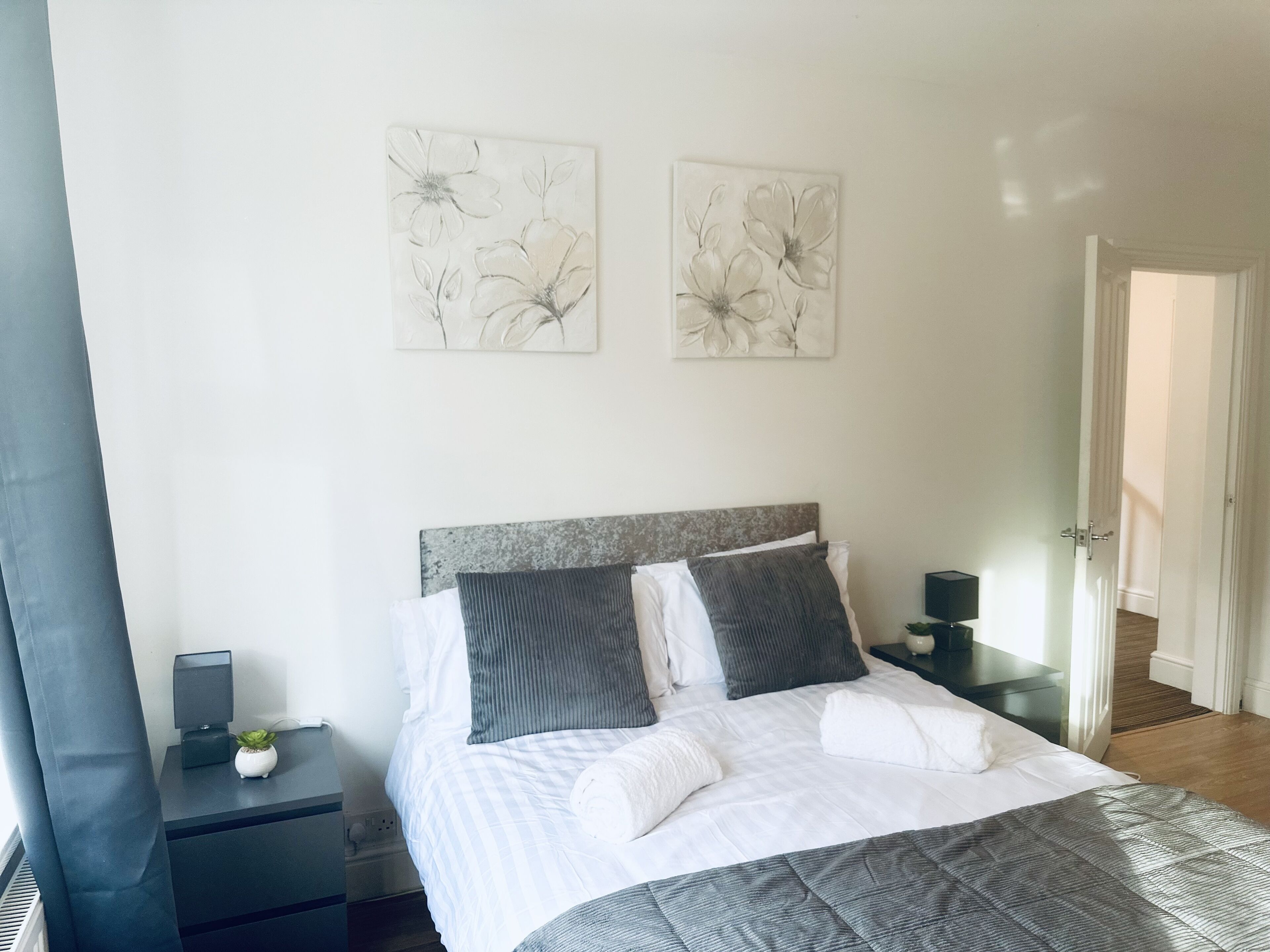 A bedroom with a bed, two nightstands, a lamp, a small plant, and two wall art pieces.