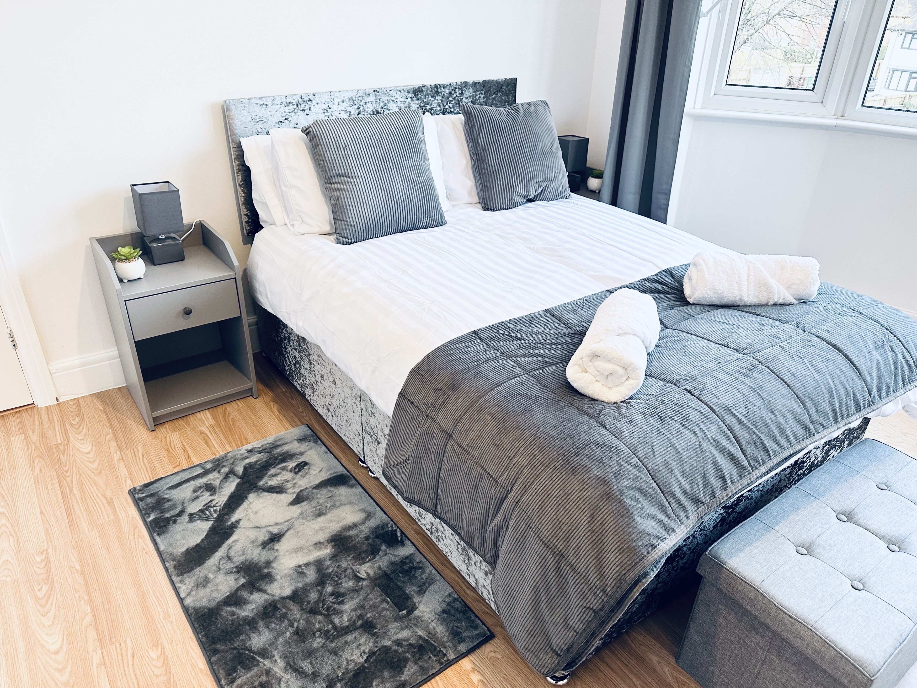 A neatly arranged bedroom with a bed, bedside tables, a rug, and a window.