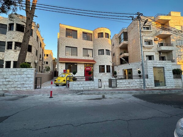 A multi-story building with a stone facade, a red door, and a yellow car parked in front.