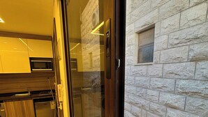 A modern kitchen with built-in appliances, a large window with a view of a stone building, and a door with a keypad lock. - Xx Antica Jabalal-lwebdeh (Amman)