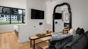 A modern living room with a large window, a flat-screen TV, a mirror, and a cozy seating area with a sofa and cushions. - Elegant Tokyo Studio , No Loadshedding (Cape Town)
