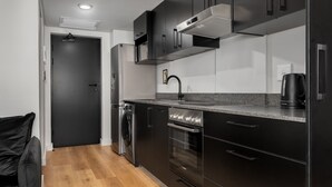 A modern kitchen with black cabinets, stainless steel appliances, and a wooden floor. - Elegant Tokyo Studio , No Loadshedding (Cape Town)
