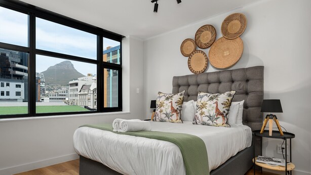 A modern bedroom with a large bed, a view of buildings and a mountain, and decorative wall art. - Elegant Tokyo Studio , No Loadshedding (Cape Town)
