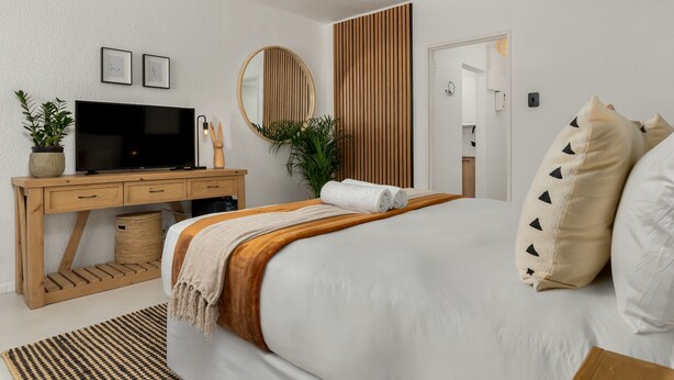 Ein modernes Schlafzimmer mit einem großen Bett, einem Holztisch, einem Fernseher und einem Spiegel.