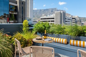 A rooftop terrace with outdoor seating, a bottle of champagne, and a view of a cityscape with a mountain in the background.