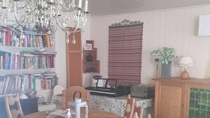 Un comedor con una mesa de madera, sillas, una lámpara de araña, una estantería y una ventana con persianas.