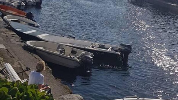 Un puerto deportivo con barcos amarrados a lo largo de la costa, un cielo despejado y edificios al fondo.