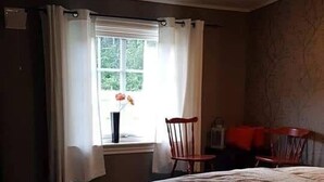 Un dormitorio con cama, ventana con cortinas, una silla y una mesita de noche.