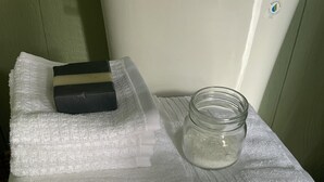 WC, jonka päällä on pino valkoisia pyyhkeitä, lasipurkki kannella ja saippuapala.