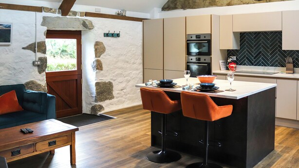 Uma cozinha moderna com parede em pedra, vigas de madeira e uma ilha embutida com banquetas.