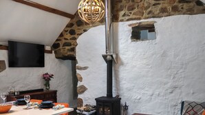 Uma sala de estar acolhedora com parede de pedra, lareira, mesa de madeira e poltrona azul.