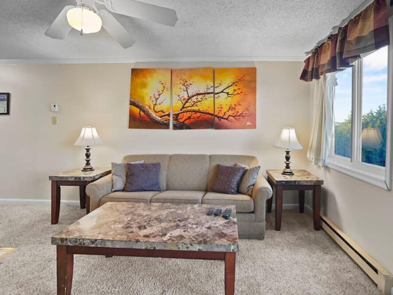 A living room with a sofa, coffee table, and two side tables with lamps. A large painting is on the wall above the sofa.
