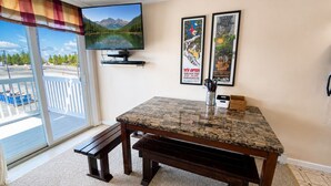 Una habitación con televisión, una mesa con cubierta de granito, un banco y vista a una montaña a través de una ventana.