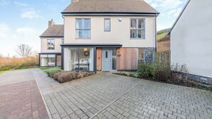 Une maison moderne à deux étages, dotée d’une allée pavée, de grandes fenêtres et d’une clôture en bois.